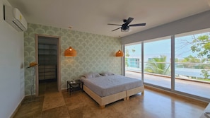 A bedroom with a bed, two pendant lights, a ceiling fan, and a large window with a view of palm trees and buildings. - Espectacular casa de playa (Juan de Acosta)