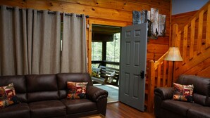 Interior acogedor de una cabaña con un sofá de cuero marrón, una pequeña mesa de madera y una puerta que da a una terraza exterior.