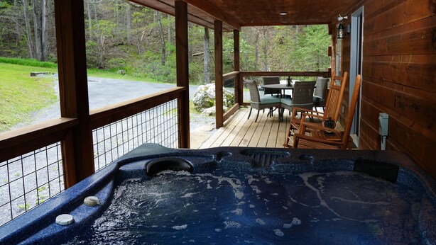 Una terraza de madera con jacuzzi, mobiliario exterior y vistas al bosque circundante.