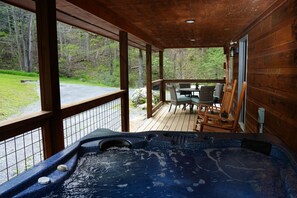 Eine Holzterrasse mit Whirlpool, Sitzgelegenheiten und Blick auf den umliegenden Wald.