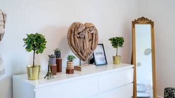 Un aparador blanco con adornos, incluyendo una escultura con forma de corazón, marcos de fotos y pequeñas macetas.