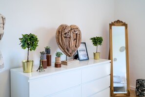 Une commode blanche agrémentée d’objets décoratifs, notamment une sculpture en forme de cœur, des photos encadrées et de petites plantes en pot.