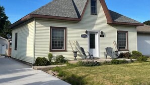 A single-story house with a gabled roof, a front door, and a small porch with two chairs.