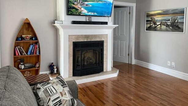 A living room with a fireplace, a television mounted above it, a bookshelf, and a painting on the wall.
