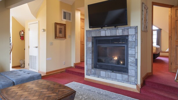 A living room with a stone fireplace, a flat-screen TV mounted above it, a blue sofa, and a herringbone-patterned coffee table. - Spacious Private Suite with full kitchen, private deck and pet friendly! (Blowing Rock)