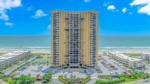 A high-rise hotel with multiple floors, a parking lot, and a beach view. - Experience Coastal Luxury: 2-Bedroom Oceanfront Condo in Myrtle Beach! (Myrtle Beach)