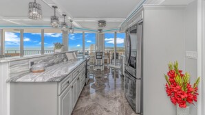 A modern kitchen with a marble countertop, stainless steel appliances, and large windows offering a view of the ocean. - Experience Coastal Luxury: 2-Bedroom Oceanfront Condo in Myrtle Beach! (Myrtle Beach)