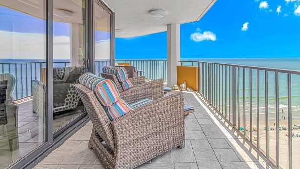 A balcony with wicker furniture and a glass door leading to a beach view. - Experience Coastal Luxury: 2-Bedroom Oceanfront Condo in Myrtle Beach! (Myrtle Beach)