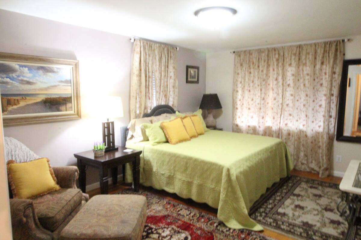A bedroom with a bed, a chair, a nightstand, a lamp, and a painting on the wall.