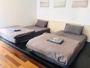 Two single beds with grey bedding and pillows, a wooden floor, and a white wall with three framed pictures. - Shade House - Phuket Downtown (Ratsada)