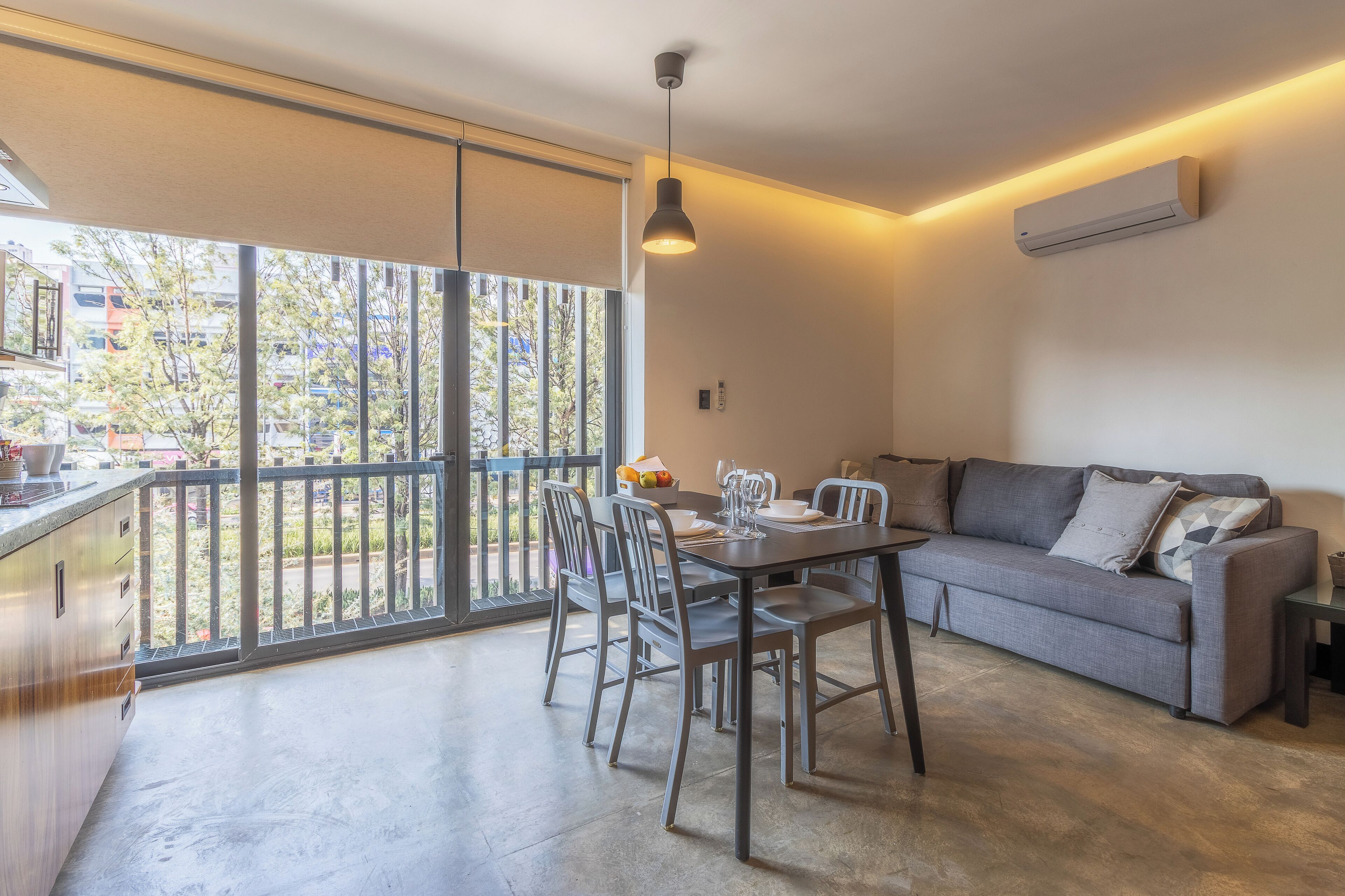 A modern living room with a dining area, large sliding glass doors to a balcony, and a built-in air conditioning unit.