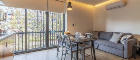 A modern living room with a dining area, large sliding glass doors to a balcony, and a built-in air conditioning unit.