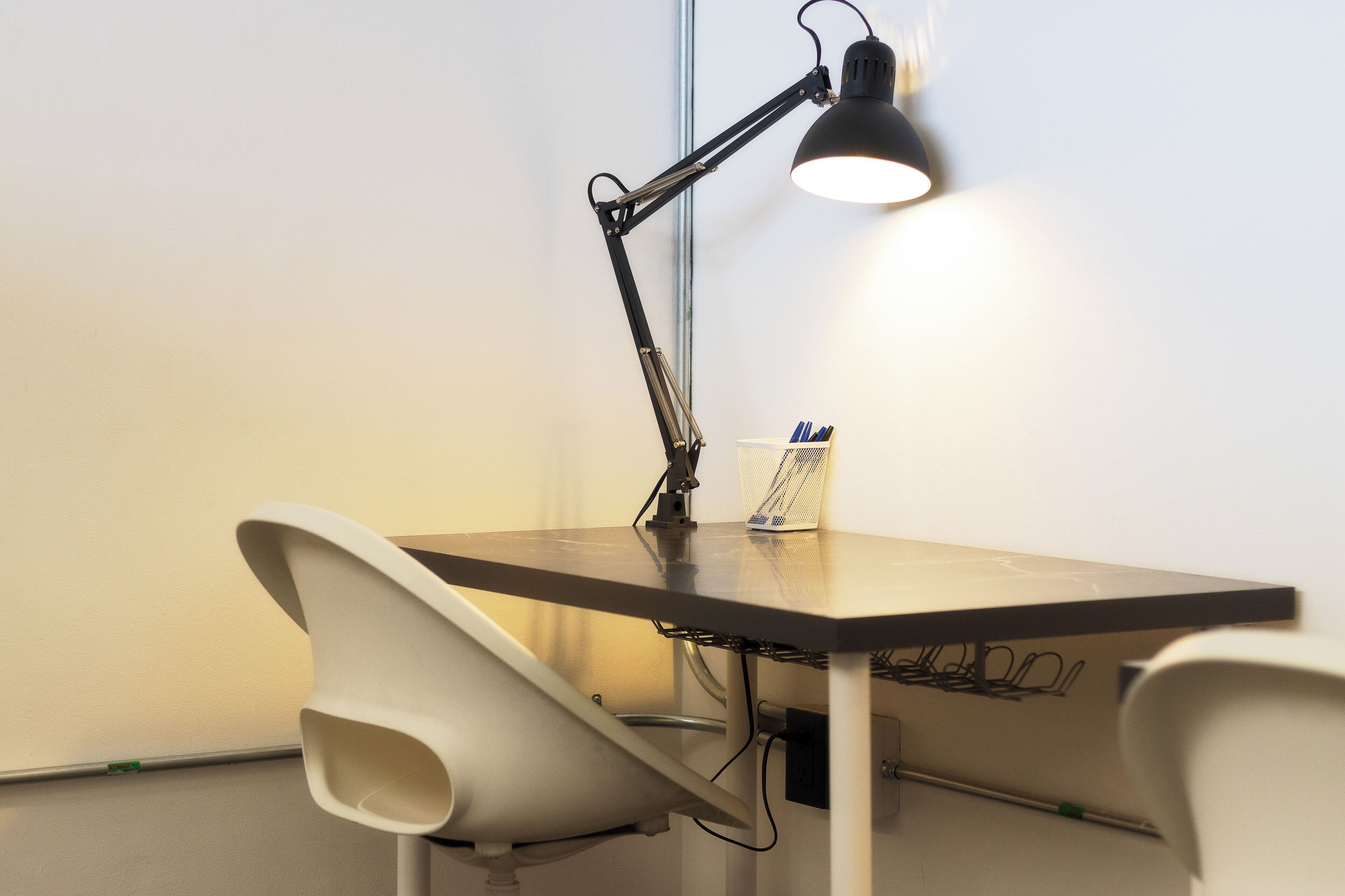 A modern workspace with a desk, two chairs, a desk lamp, and a cup holder with pens.