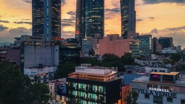 Un paisaje urbano con modernos rascacielos, una calle con un coche y un edificio con el rótulo 