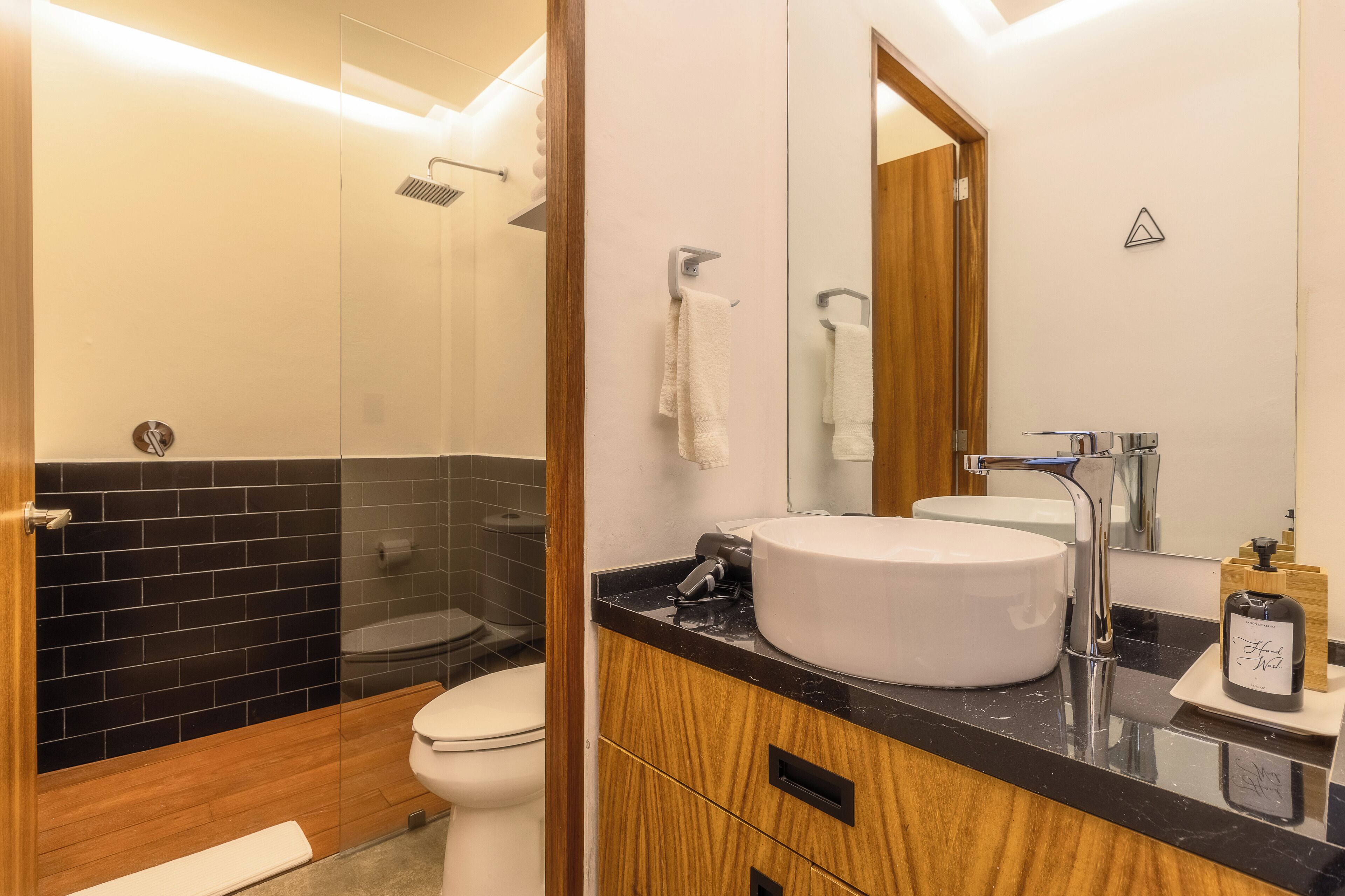 Une salle de bain moderne avec une douche à l’italienne en verre, un lavabo blanc et un meuble-lavabo en bois.