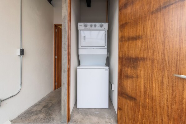 Un lavadero pequeño con lavadora y secadora apiladas, una puerta de madera y un enchufe en la pared.