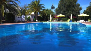 Ein Swimmingpool mit klarem, blauem Wasser, umgeben von Palmen und gelben Sonnenschirmen.