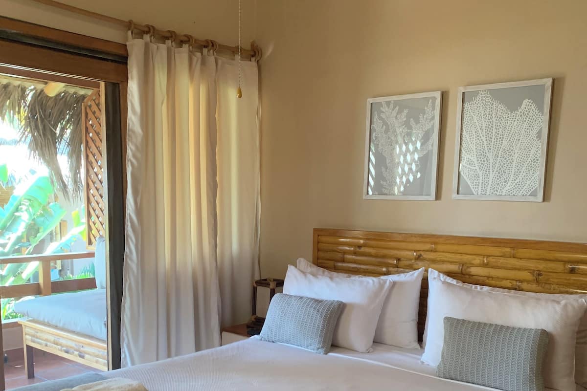 A neatly made bed with white linens and a grey throw, a wooden headboard, and two framed wall art pieces.