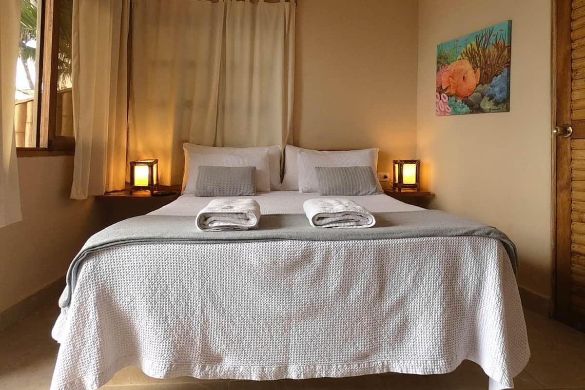 A bedroom with a bed, two bedside lamps, a painting on the wall, and a window with curtains.