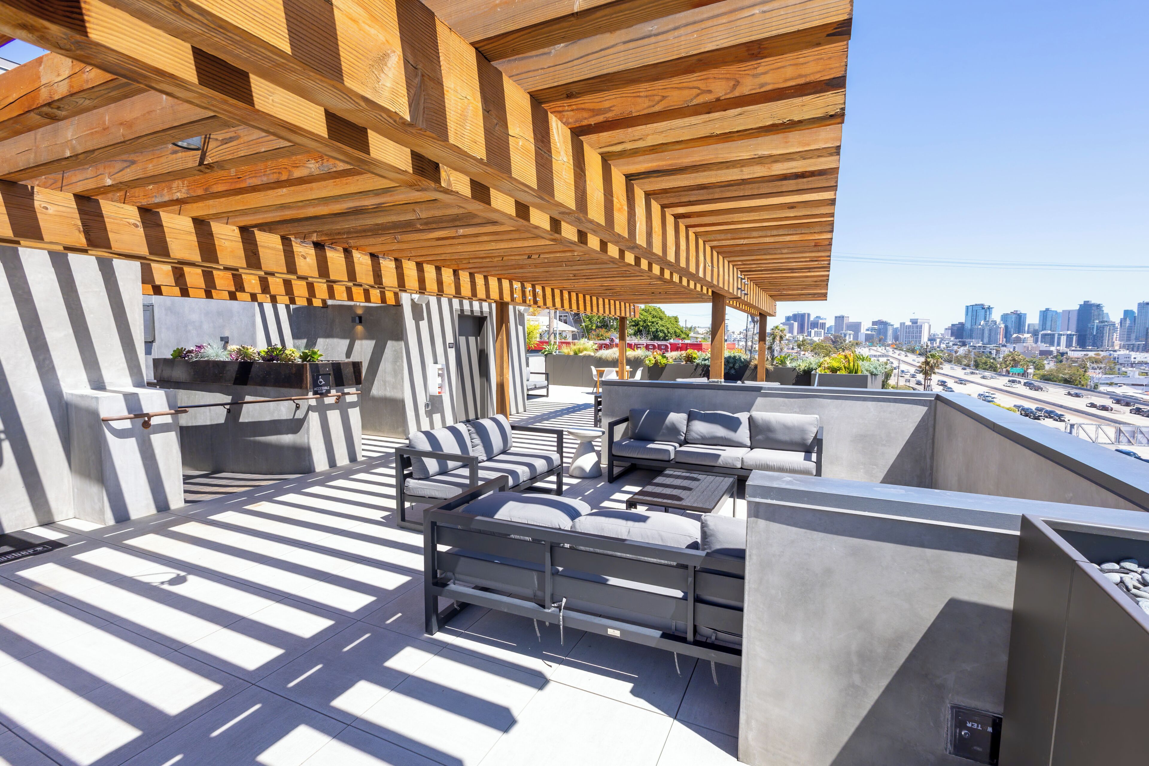 An outdoor patio with a modern design, featuring a wooden ceiling, grey seating, and a city skyline view.