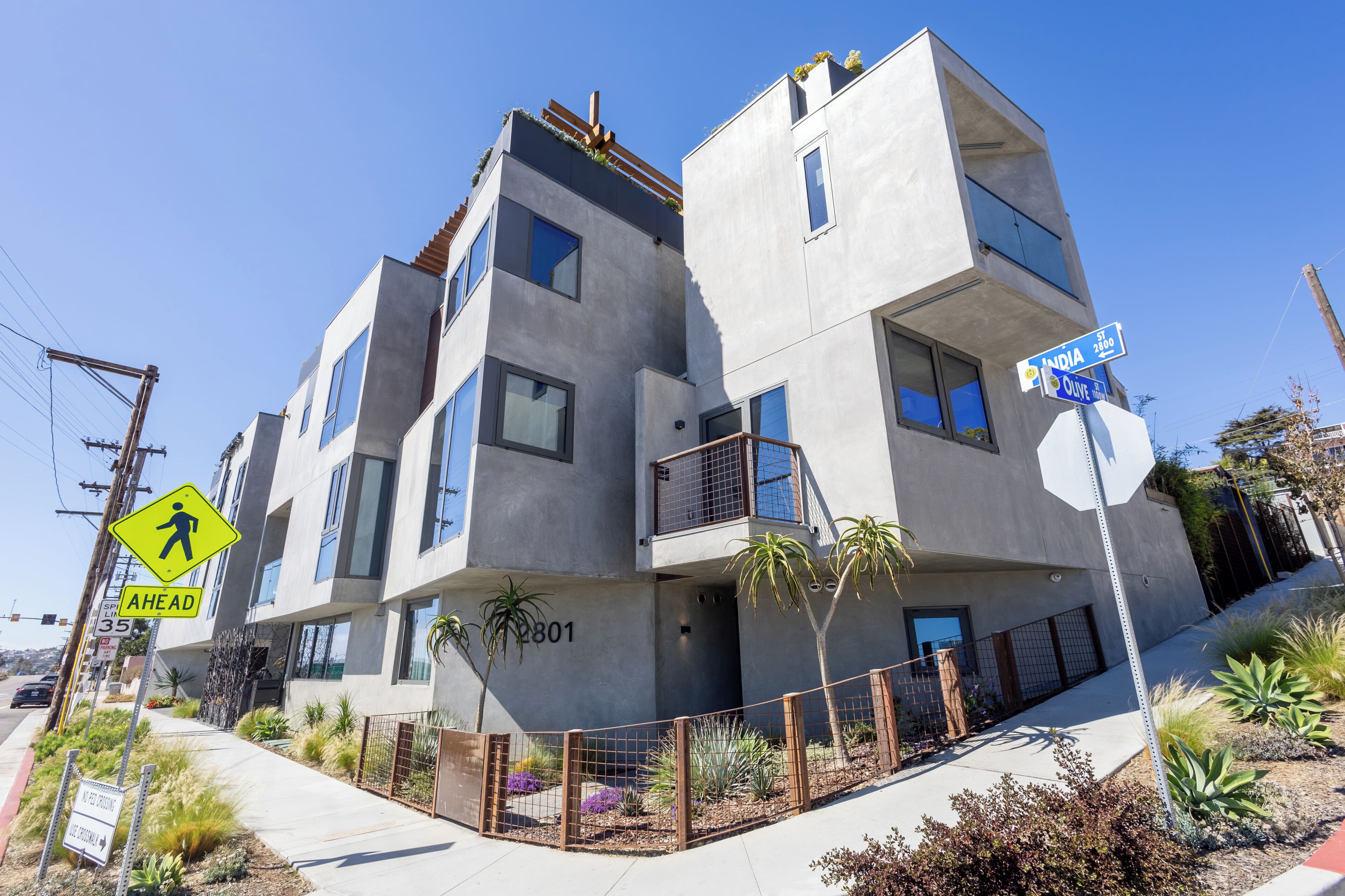 Un edificio moderno de varios pisos con balcones, una señal de paso para peatones y carteles de calle.