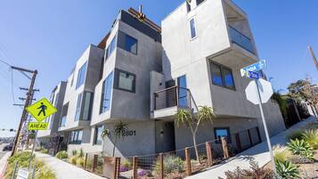 Un edificio moderno de varios pisos con balcones, una señal de paso para peatones y carteles de calle.
