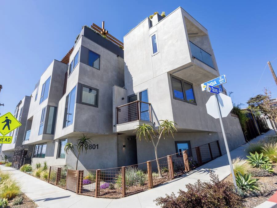 Un edificio moderno de varios pisos con balcones, una señal de paso para peatones y carteles de calle.