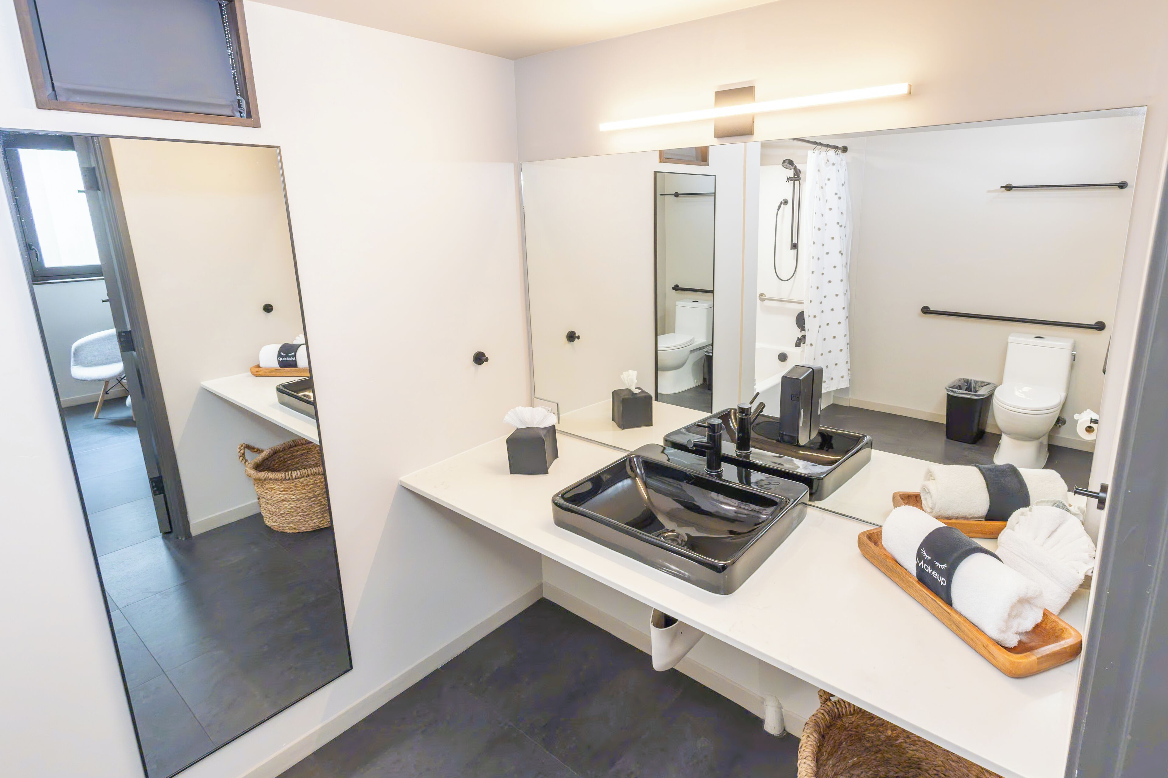 A modern bathroom with a large mirror, a sink with a black basin, and a shower area.