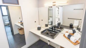 A modern bathroom with a large mirror, a sink with a black basin, and a shower area.