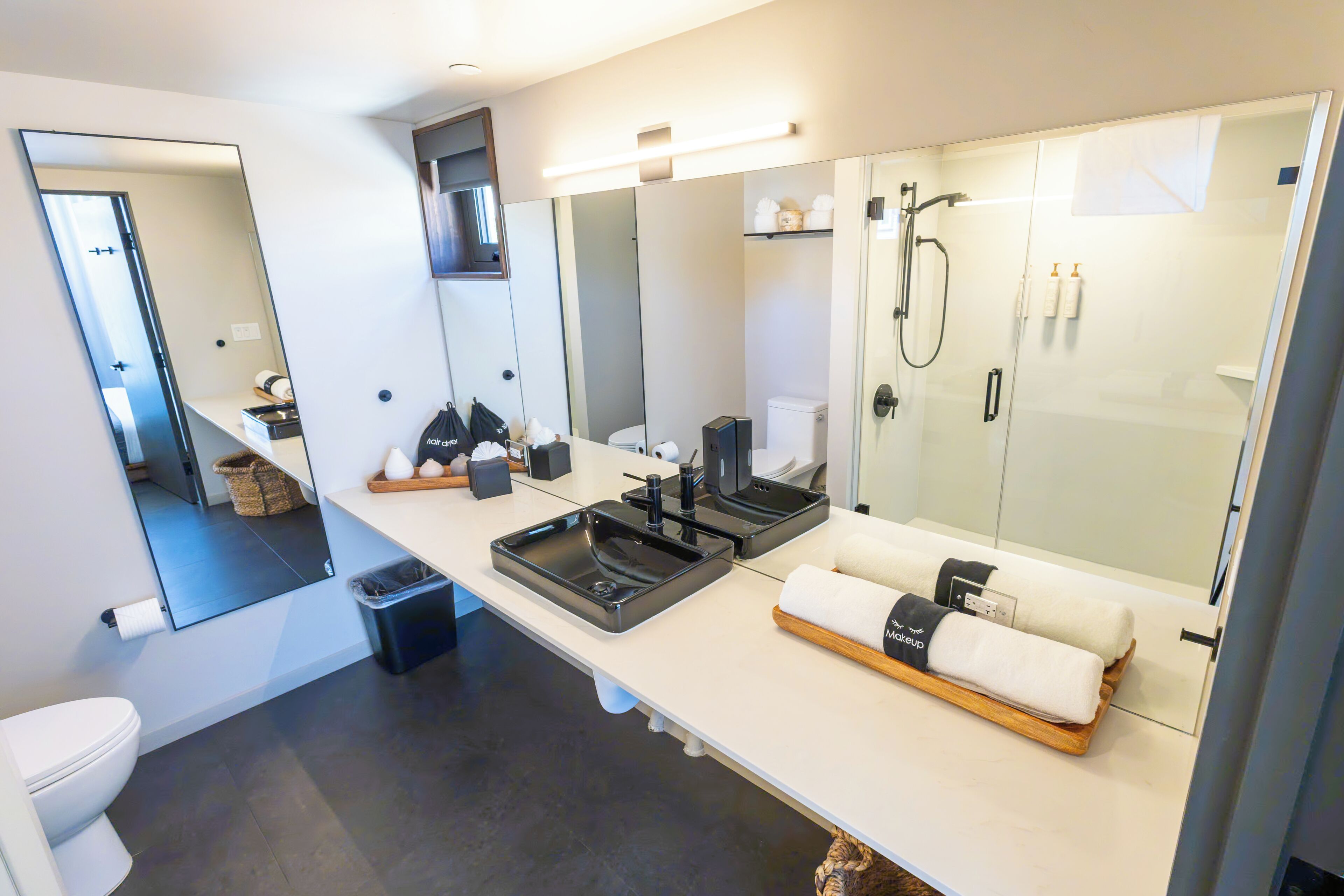 A modern bathroom with a large mirror, two sinks, a shower, and a towel rack.