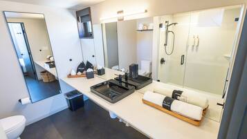 A modern bathroom with a large mirror, two sinks, a shower, and a towel rack.