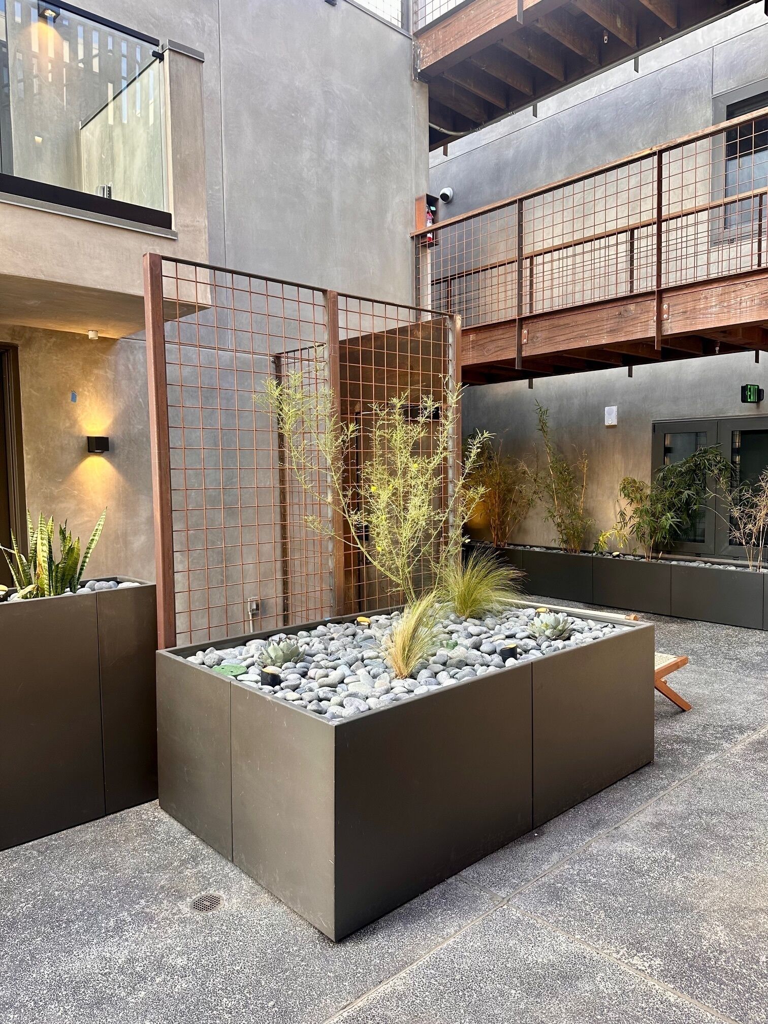 Un jardin intérieur moderne, doté d’une clôture en métal, de jardinières contenant diverses plantes et d’un sol en béton.