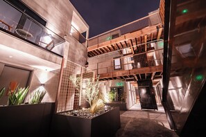 Un edificio moderno con un patio central, destacando una jardinera con plantas, una escalera y una barandilla metálica.