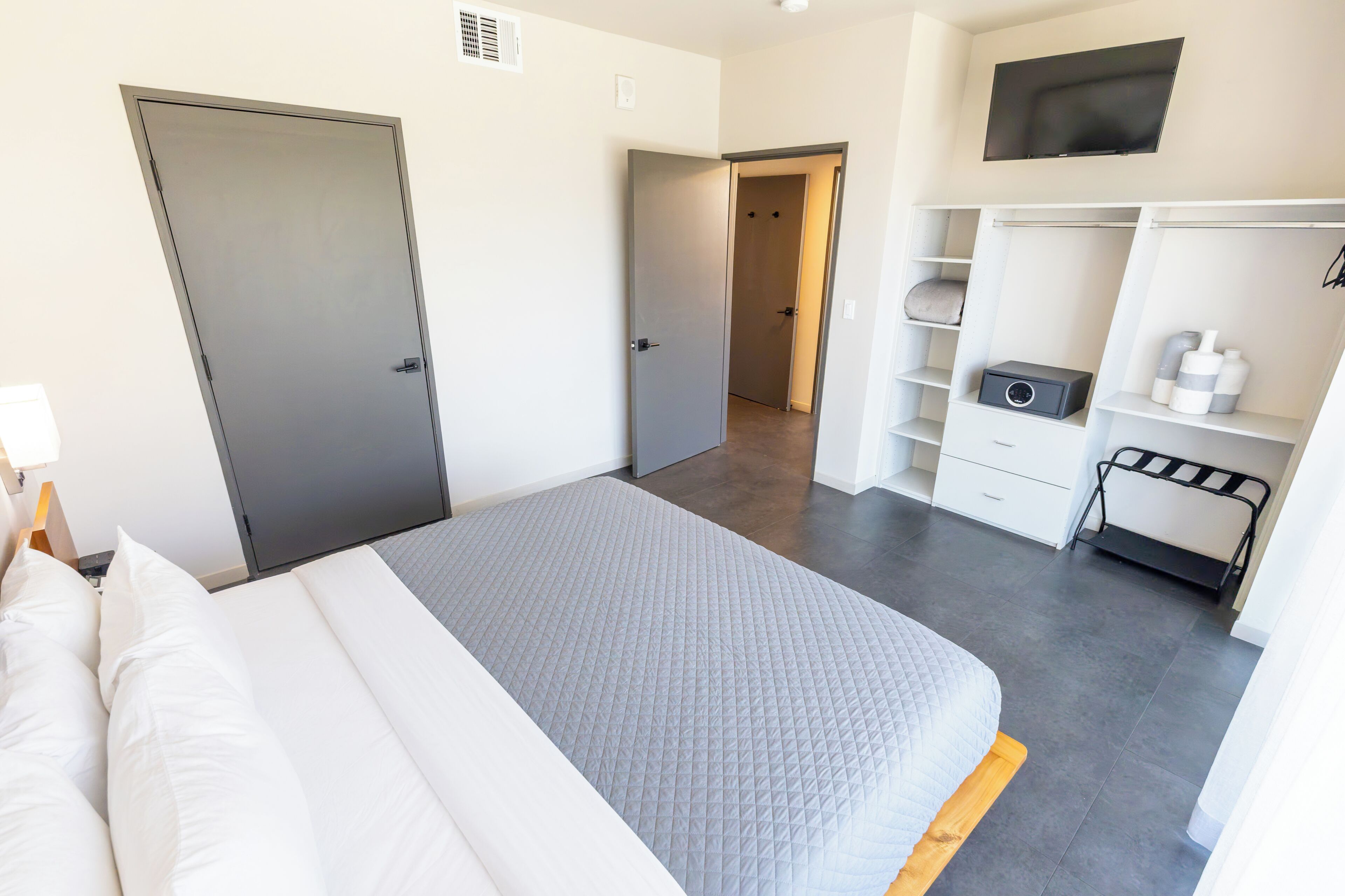 Quarto de hotel com cama, guarda-roupa, escrivaninha e televisão.