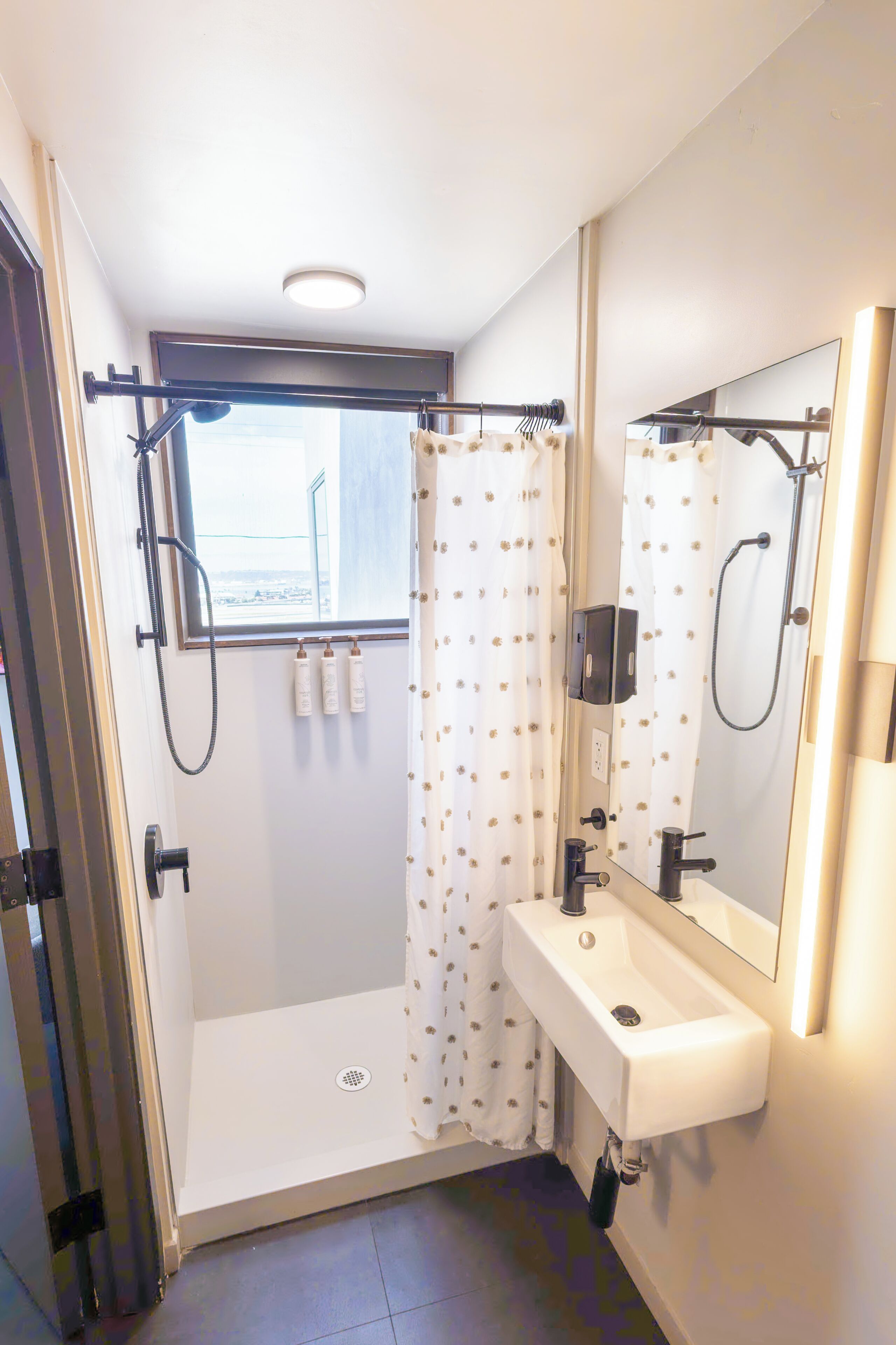 A bathroom with a shower, a sink, a mirror, and a window.