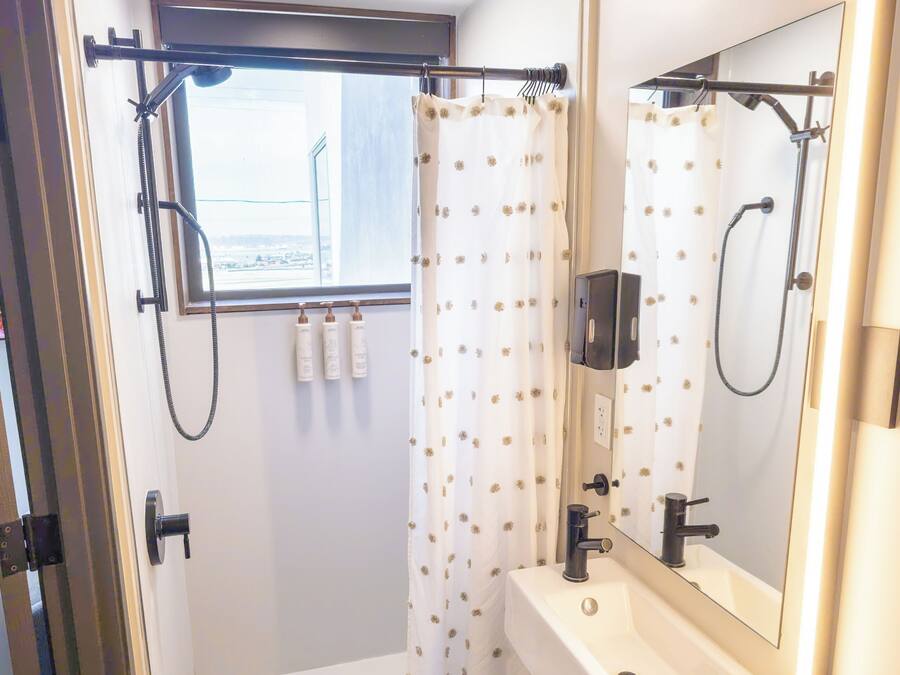 A bathroom with a shower, a sink, a mirror, and a window.