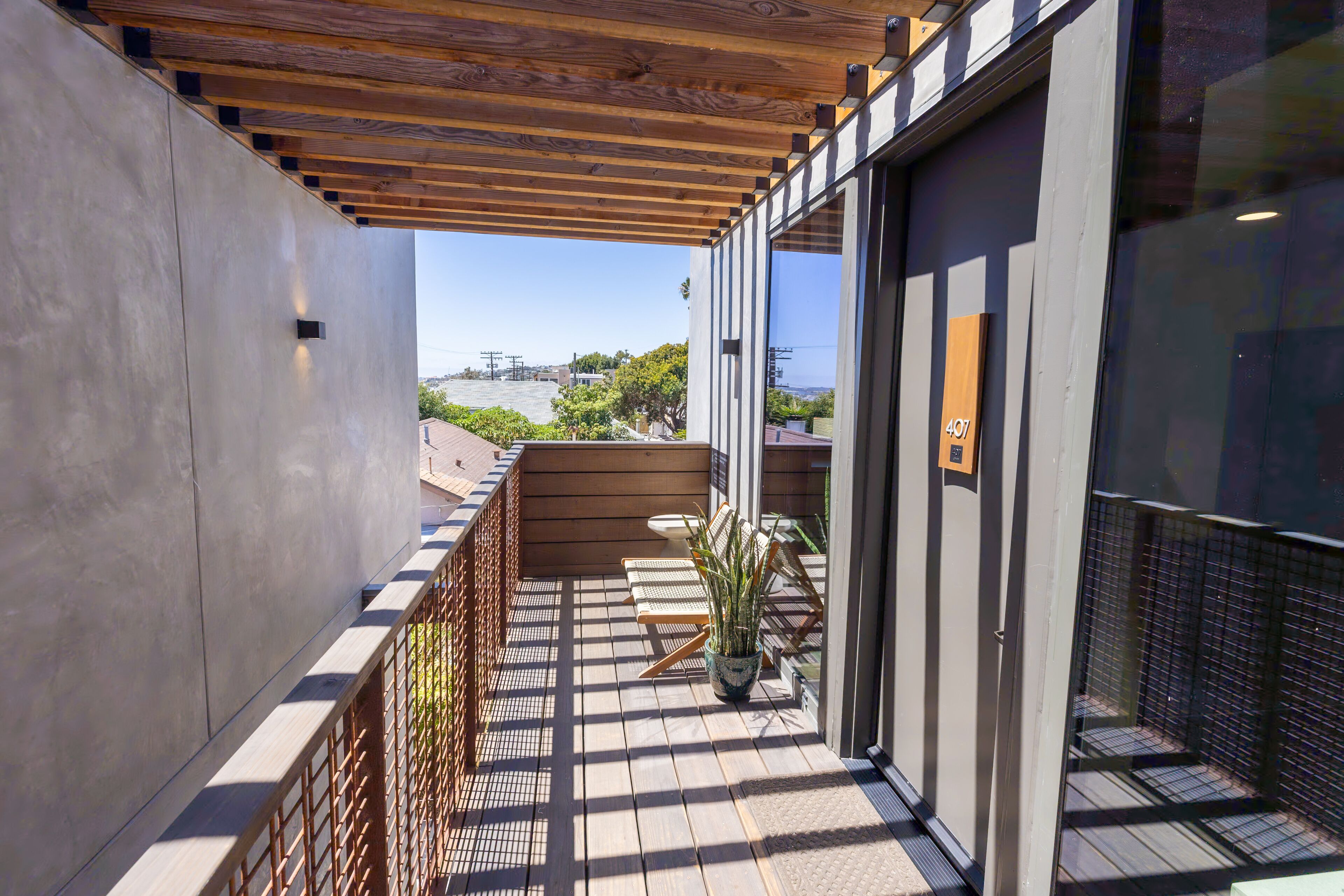 A balcony with a wooden railing, a potted plant, and a view of the cityscape.