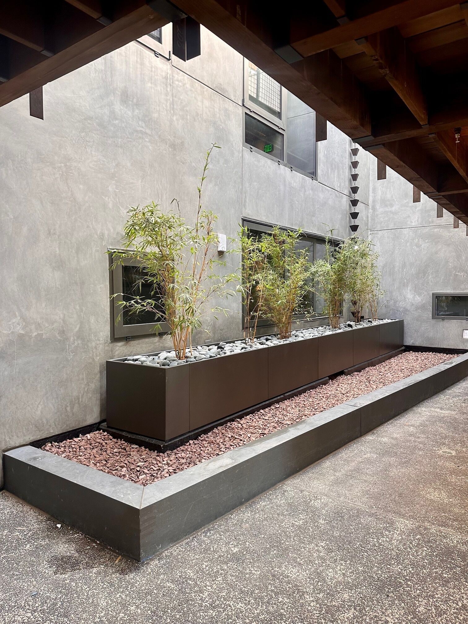 A modern outdoor area with concrete walls, a gravel pathway, and rectangular planters with plants and rocks.