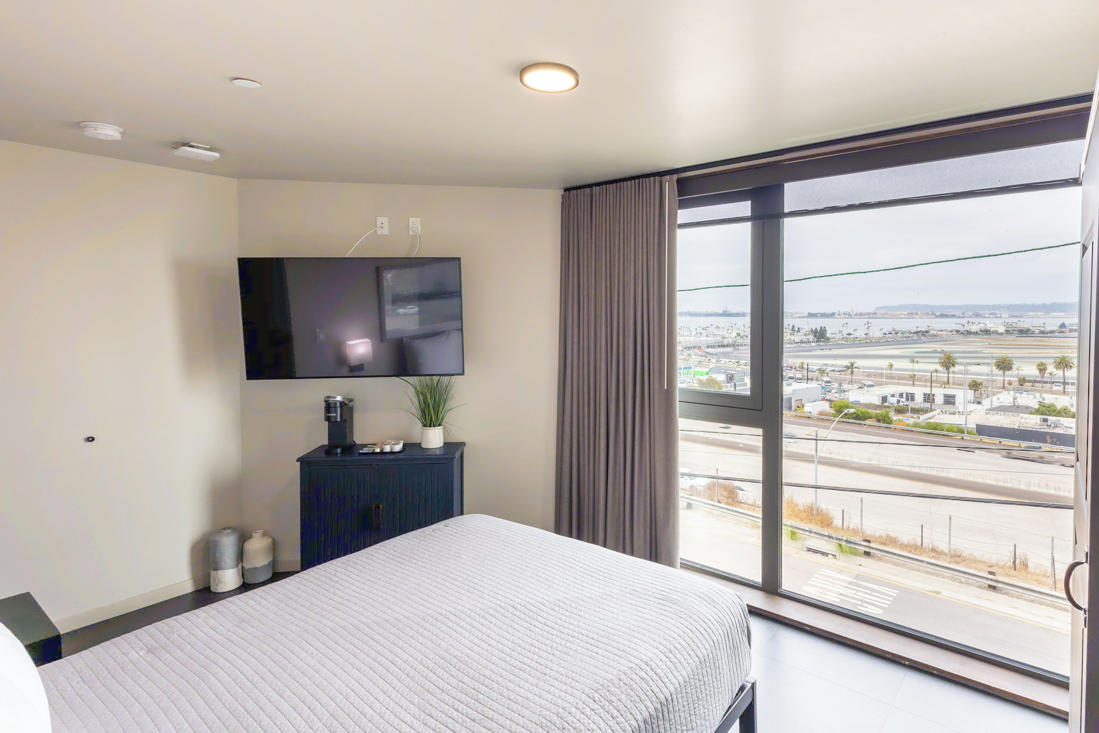 Hotelkamer met een bed, een flatscreen televisie aan de muur, een klein kastje en een raam met uitzicht op een stadsgezicht.