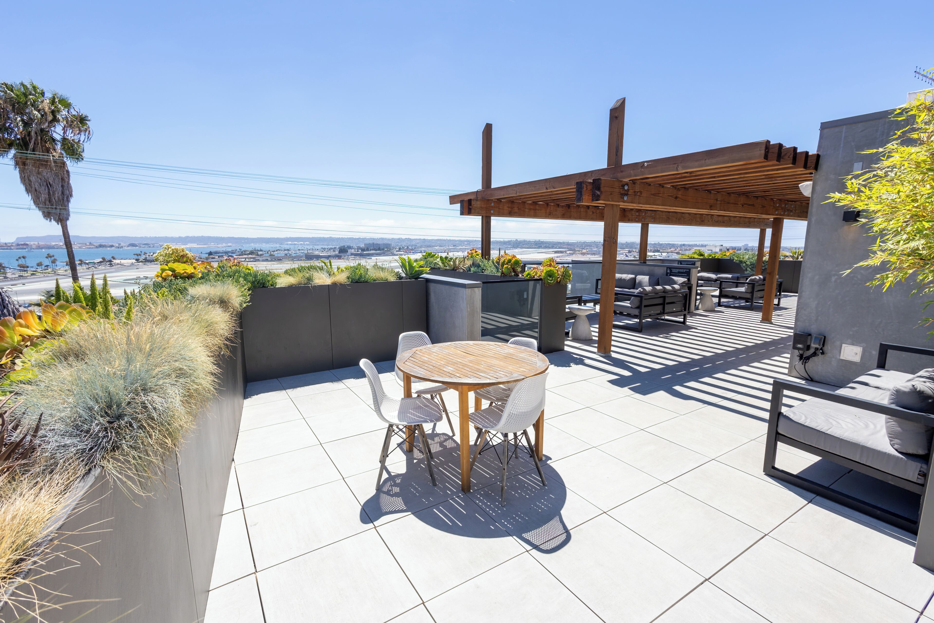 An outdoor patio with a round table and chairs, a wooden pergola, and a view of the cityscape.