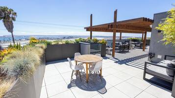 An outdoor patio with a round table and chairs, a wooden pergola, and a view of the cityscape.