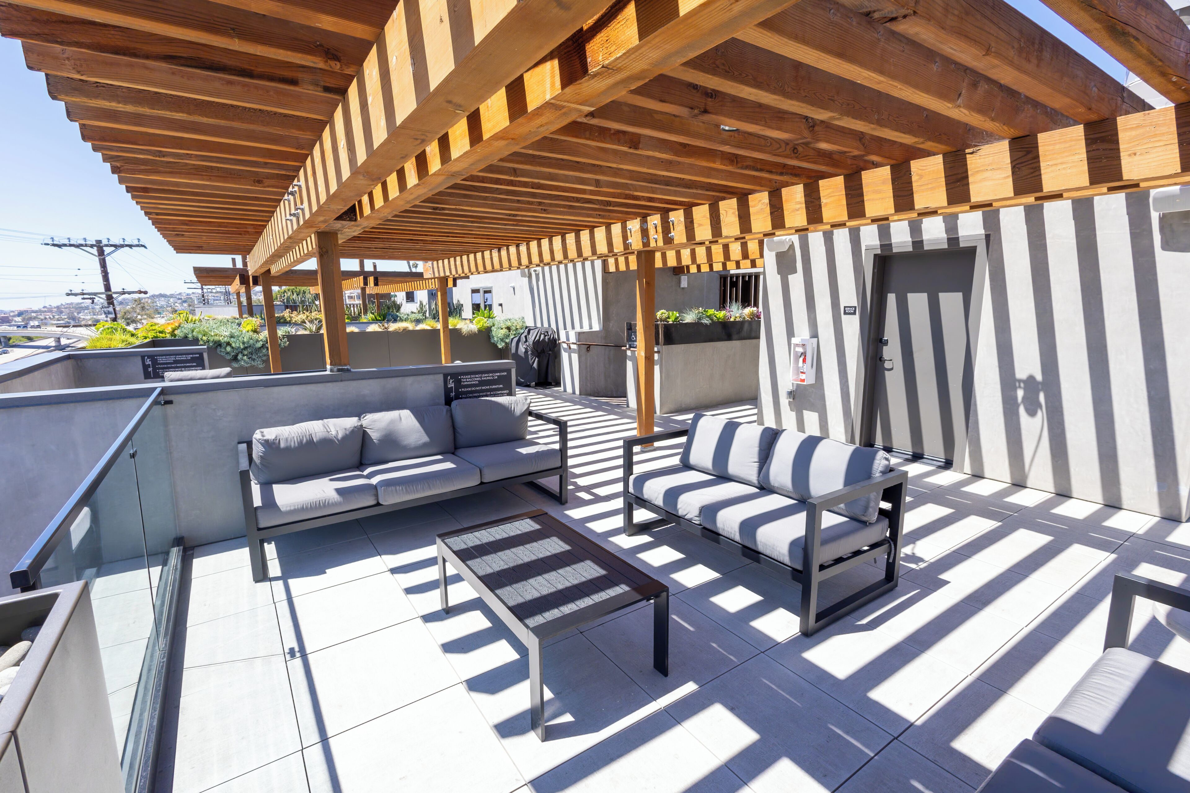 A rooftop terrace with a wooden pergola, outdoor seating, and a view of the cityscape.
