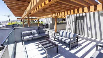 A rooftop terrace with a wooden pergola, outdoor seating, and a view of the cityscape.