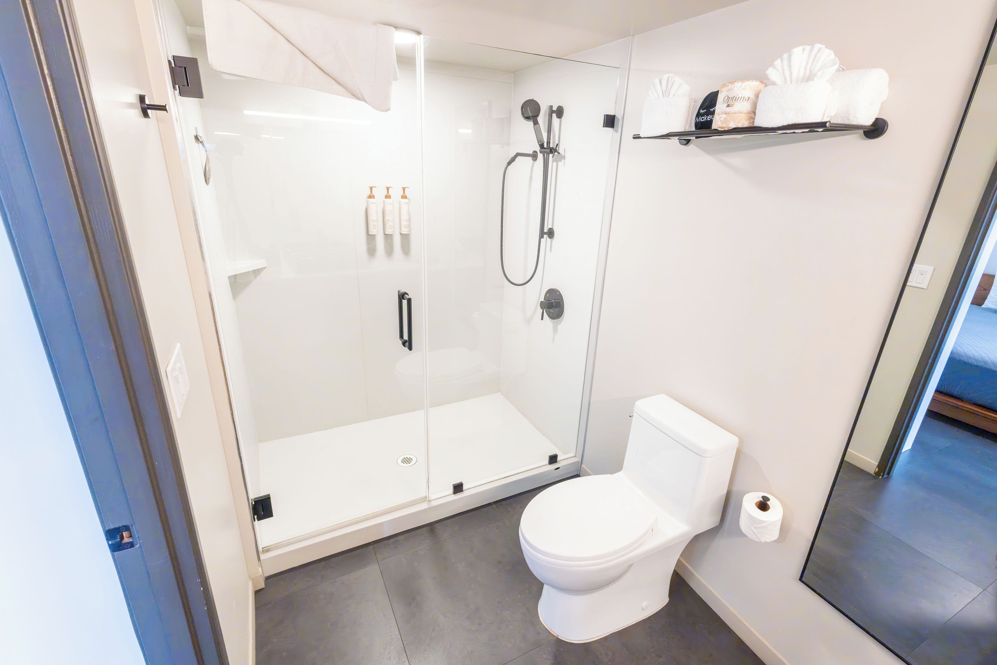 Ein modernes Badezimmer mit einer gläsernen Duschkabine, einer weißen Toilette und einem Ablagebereich für Pflegeprodukte.