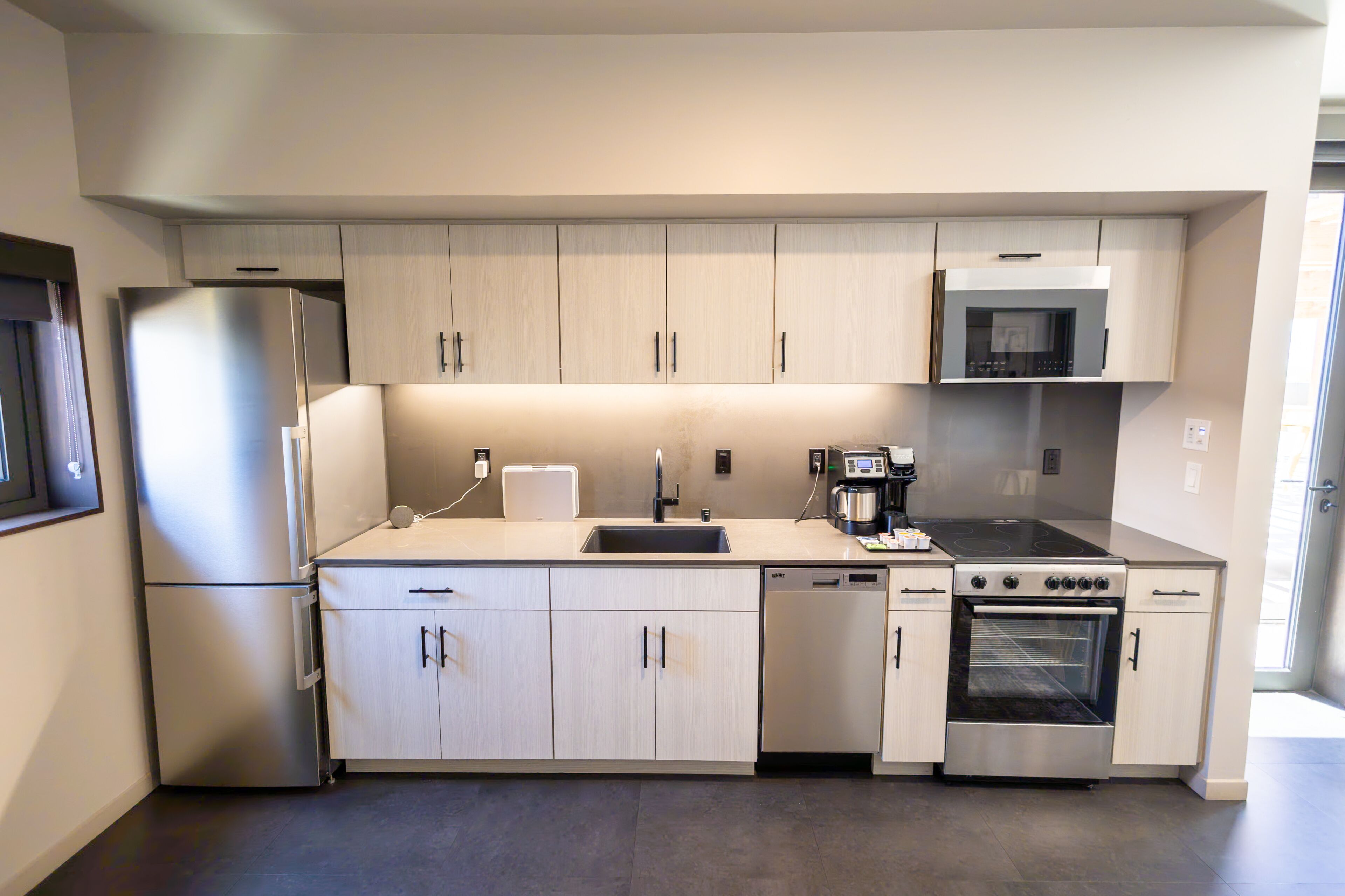 A modern kitchen with stainless steel appliances, light wood cabinetry, and a built-in oven.