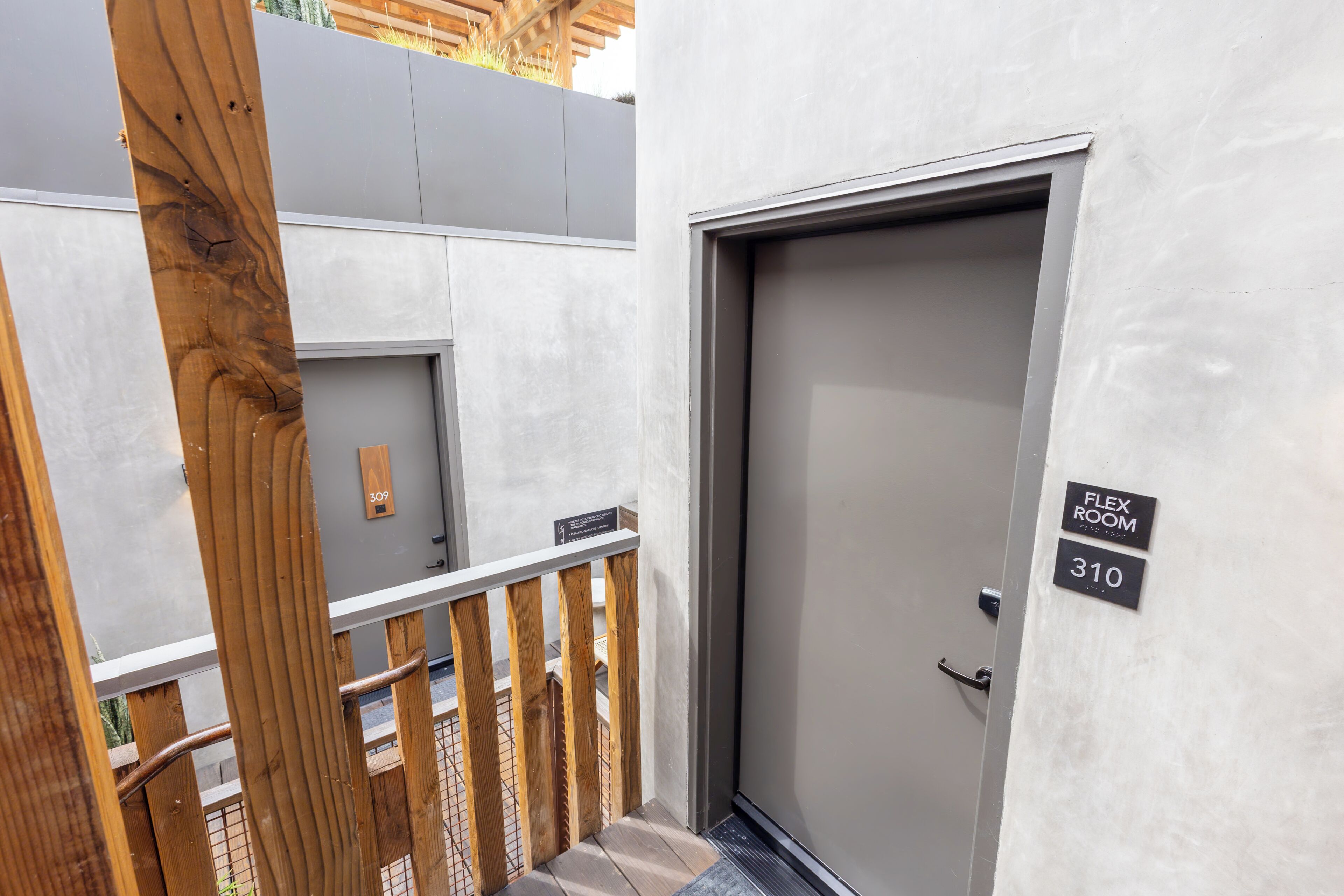 A modern building entrance with a grey door, wooden railing, and a sign indicating room numbers 309 and 310.