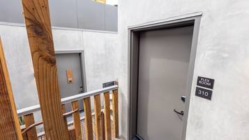 A modern building entrance with a grey door, wooden railing, and a sign indicating room numbers 309 and 310.