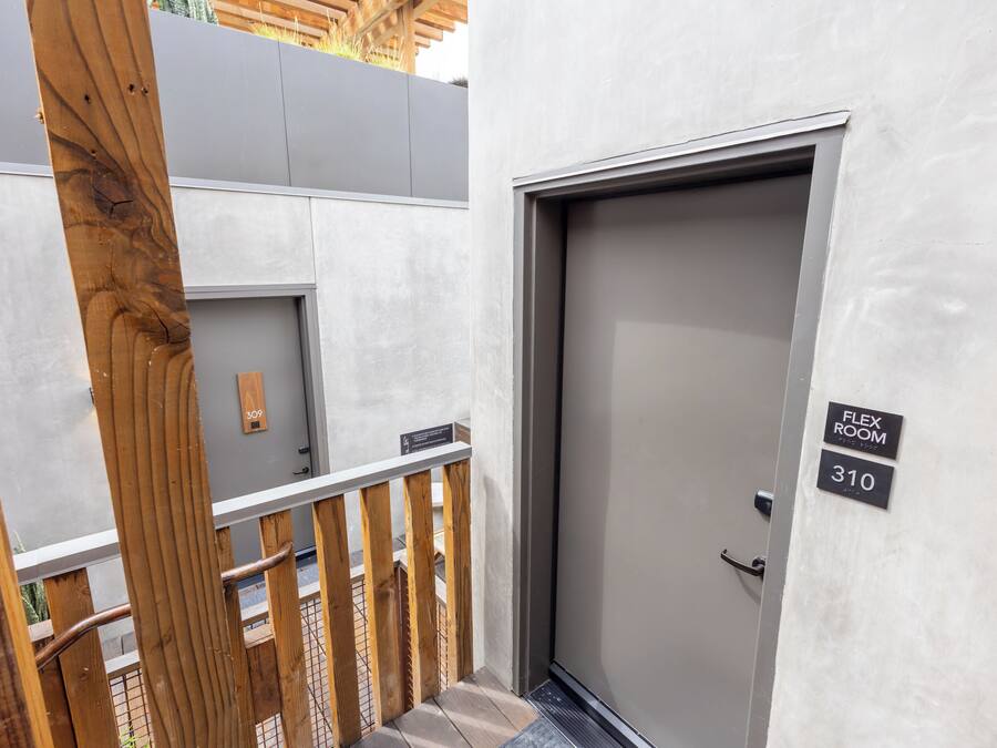 A modern building entrance with a grey door, wooden railing, and a sign indicating room numbers 309 and 310.