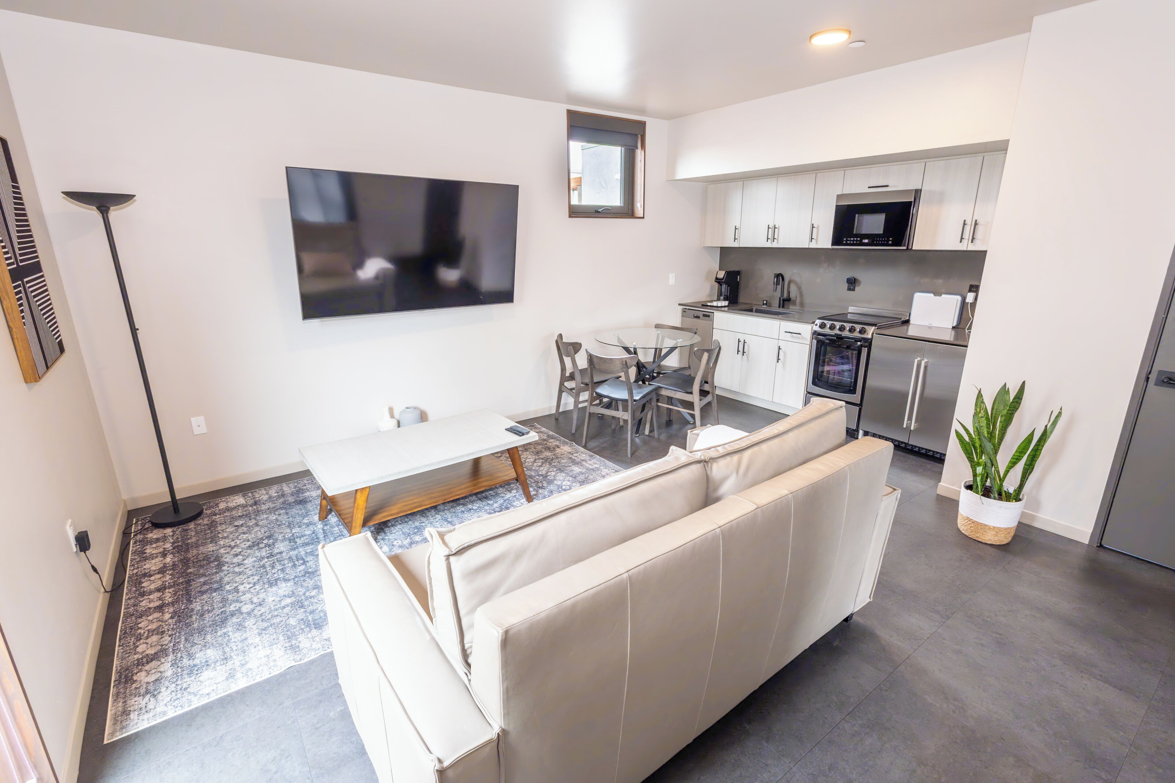 A modern kitchen with stainless steel appliances, a dining area with a glass table, and a sofa.