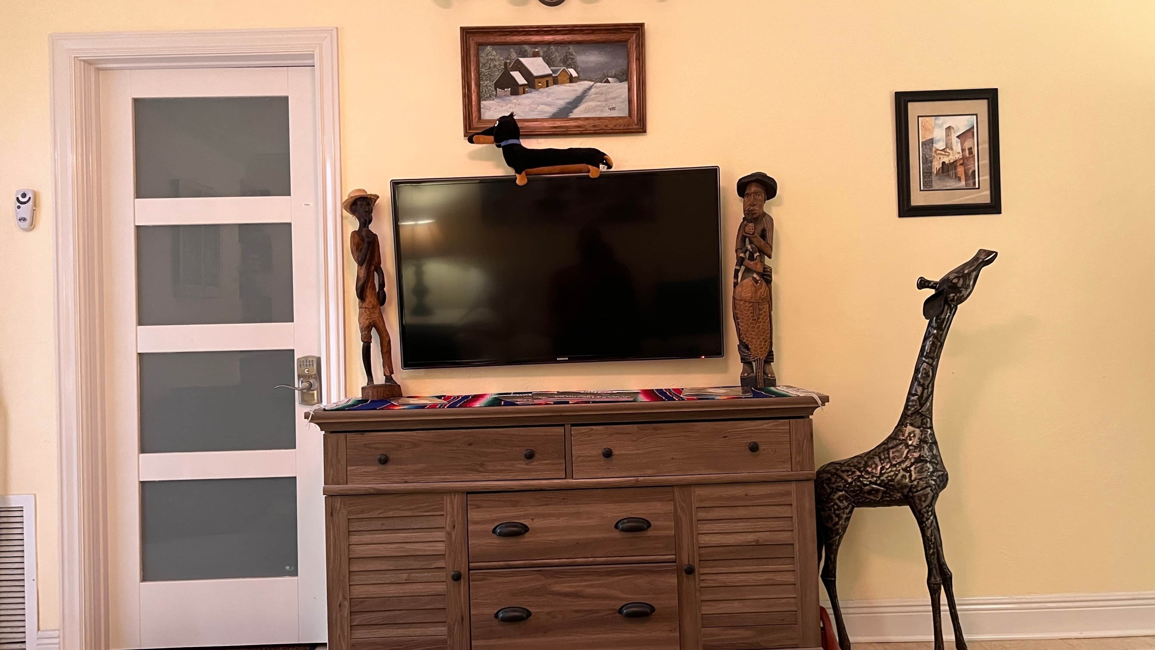 Una habitación con un televisor montado en un mueble de madera, una puerta con paneles de vidrio esmerilado y una estatua de jirafa.